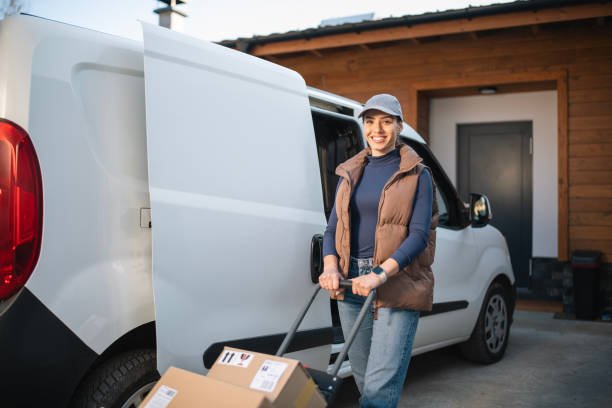 Portrait of a female courier worker standing by delivery van. Delivery worker standing by courier van looking at camera and smiling.