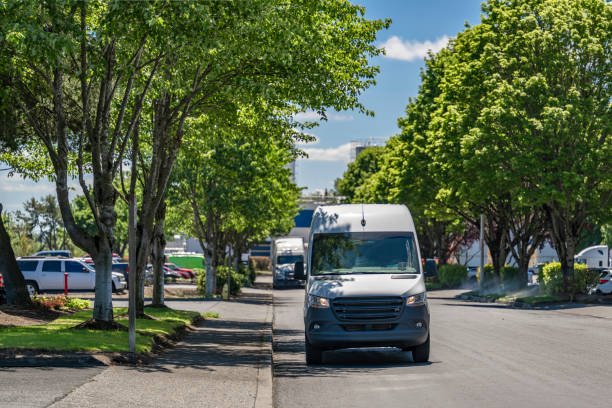 Industrial grade white compact cargo mini van for small business and local deliveries standing on the city street road in industrial commercial area with green trees